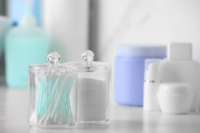 Containers with cotton swabs and pads on white countertop in bathroom, closeup. Space for text