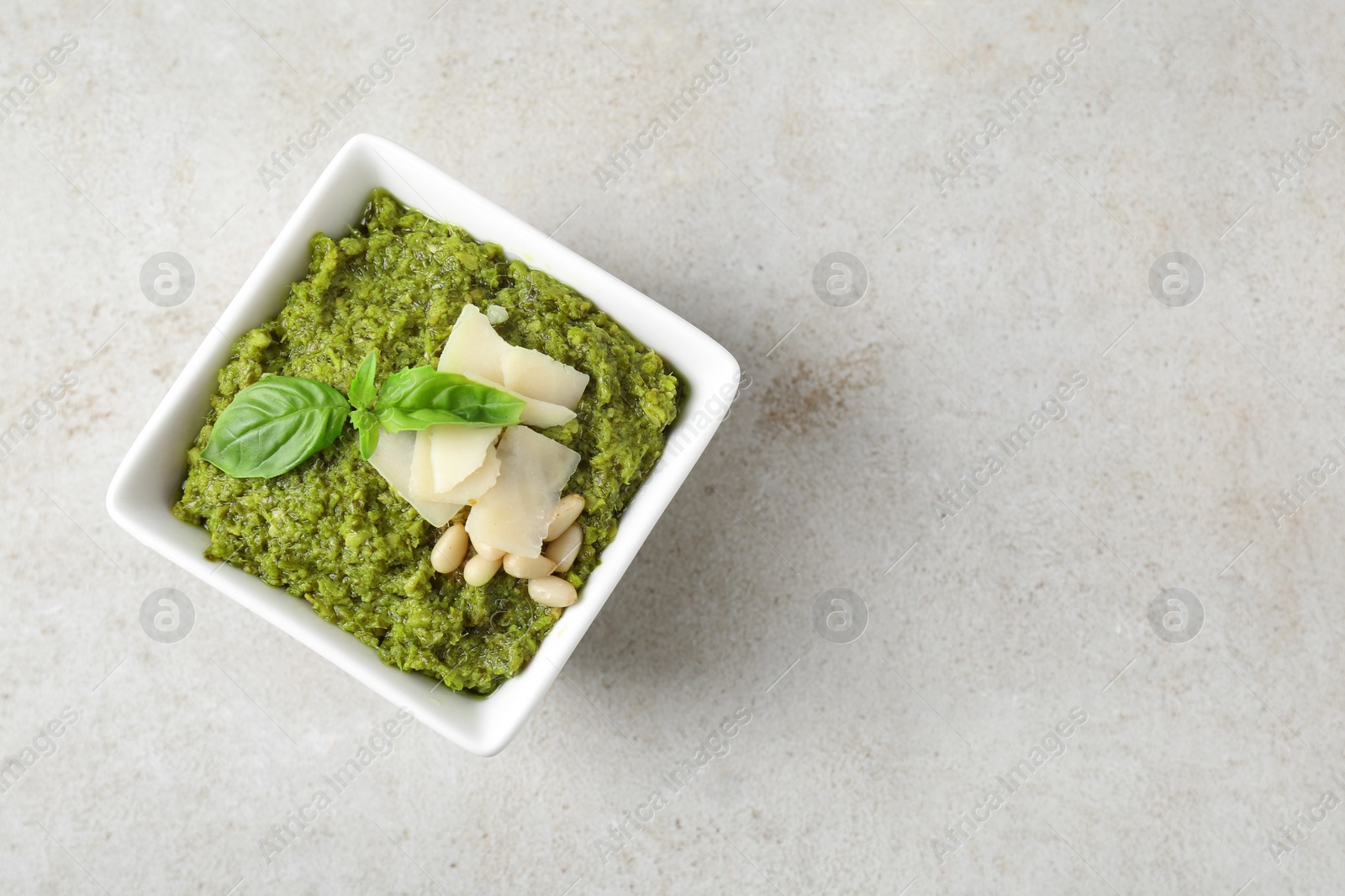 Photo of Bowl with delicious pesto sauce, cheese, pine nuts and basil leaves on light table, top view. Space for text