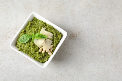 Bowl with delicious pesto sauce, cheese, pine nuts and basil leaves on light table, top view. Space for text