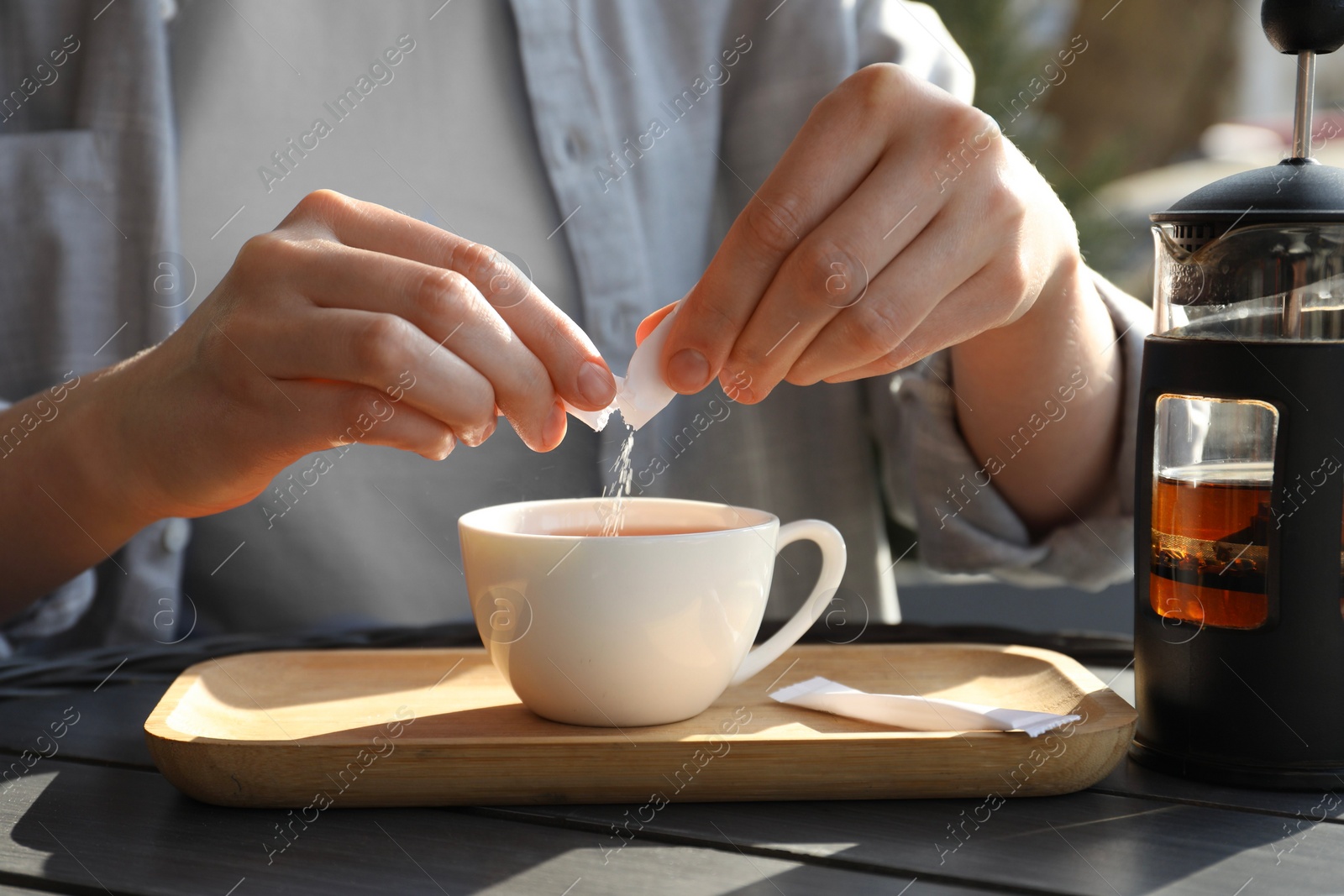 Photo of Woman adding sugar into cup of tea at black wooden table in outdoor cafe, closeup