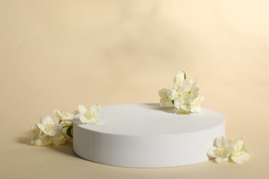 Photo of Presentation of product. White podium and beautiful jasmine flowers on beige background, space for text