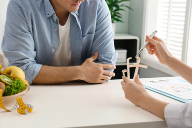 Photo of Young nutritionist consulting patient at table in clinic, closeup