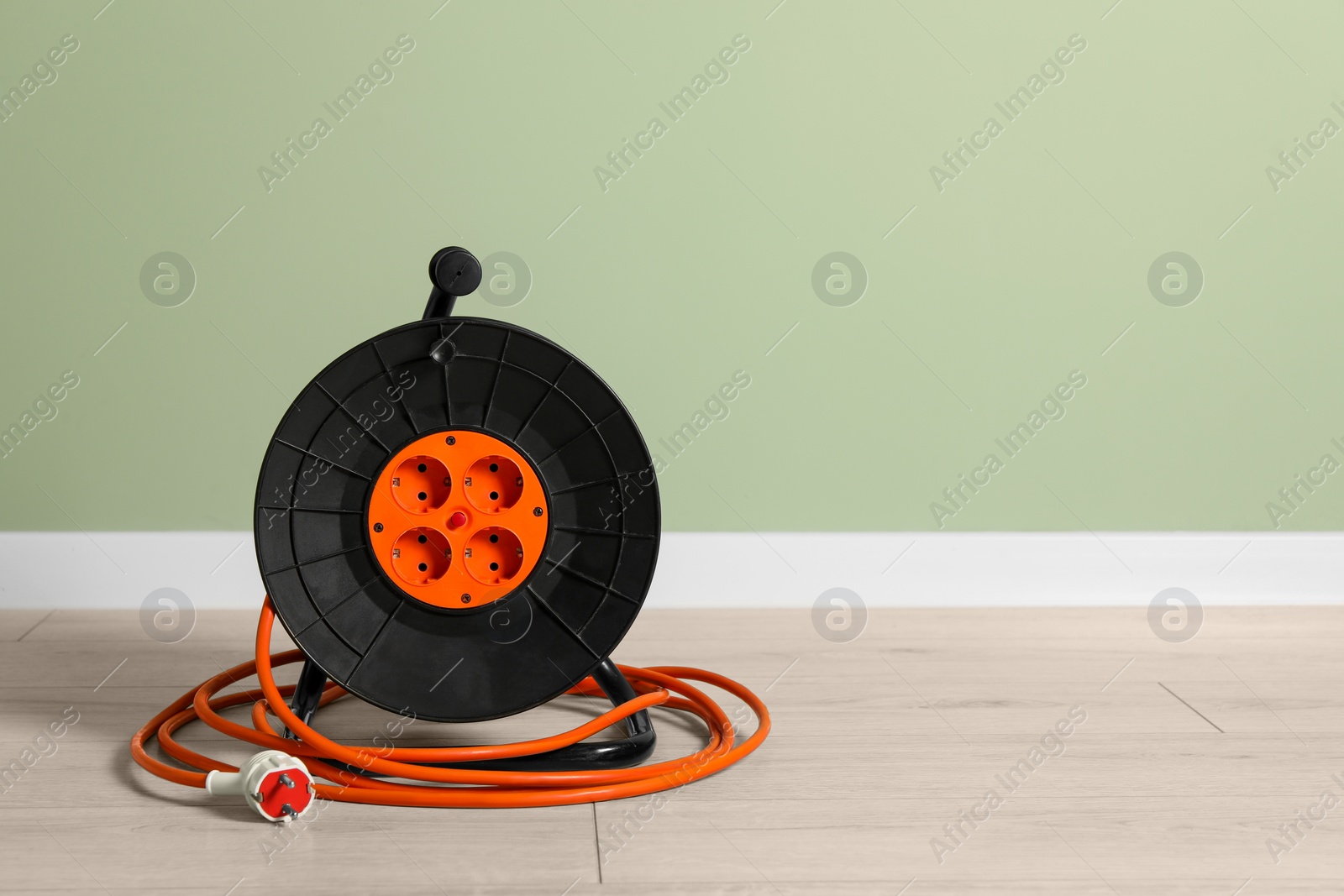 Photo of Extension cord reel on floor near light green wall, space for text. Electrician's equipment
