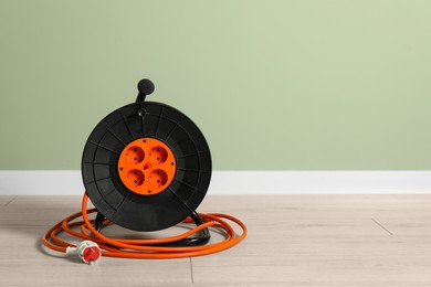 Extension cord reel on floor near light green wall, space for text. Electrician's equipment