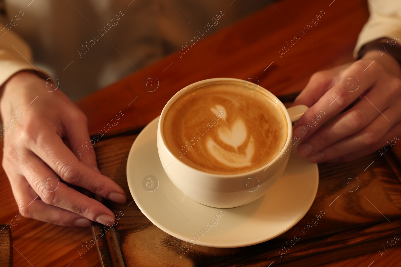 Photo of Woman with cup of aromatic coffee at wooden table, closeup