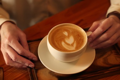 Photo of Woman with cup of aromatic coffee at wooden table, closeup