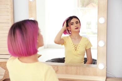 Photo of Young woman with color hair looking into mirror in beauty salon. Modern trend