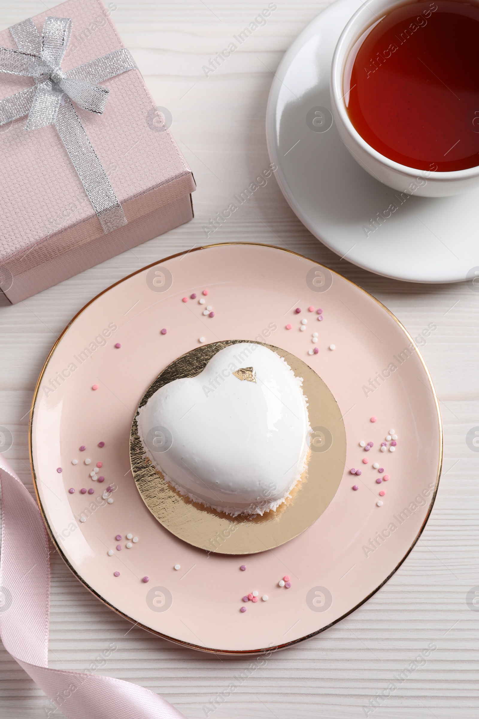 Photo of St. Valentine's Day. Delicious heart shaped cake, tea and gift on white wooden table, flat lay