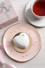 Photo of St. Valentine's Day. Delicious heart shaped cake, tea and gift on white wooden table, flat lay