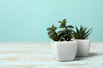 Photo of Artificial plants in white flower pots on light blue wooden table. Space for text