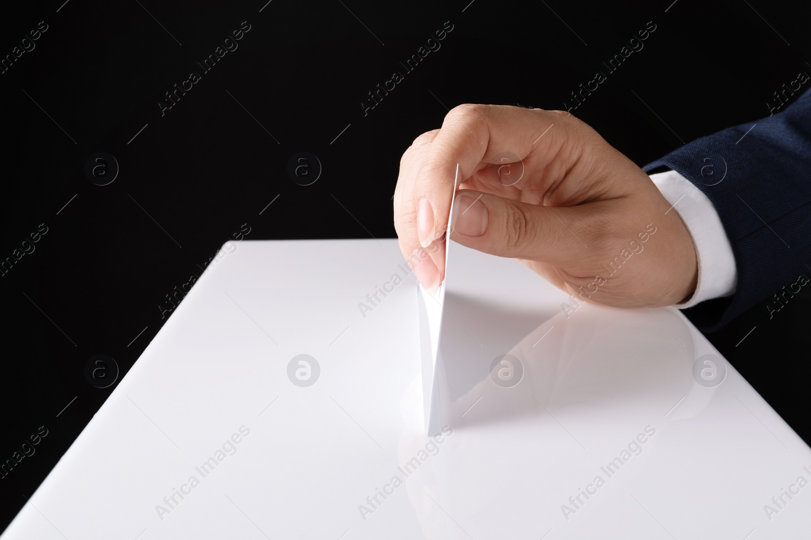 Photo of Woman putting her vote into ballot box on black background, closeup