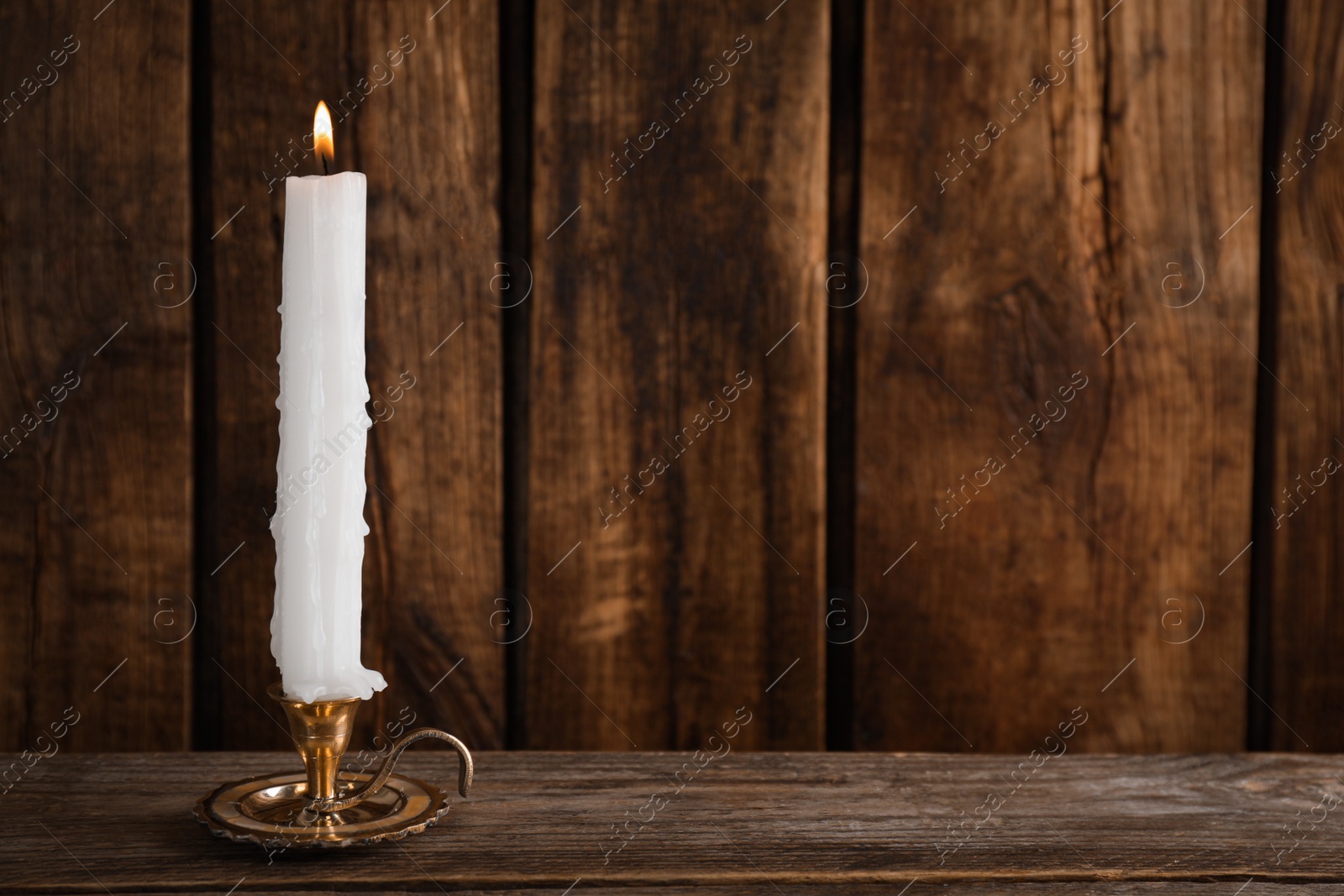 Photo of Elegant candlestick with burning candle on wooden table. Space for text