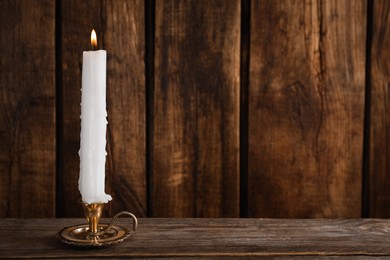 Elegant candlestick with burning candle on wooden table. Space for text