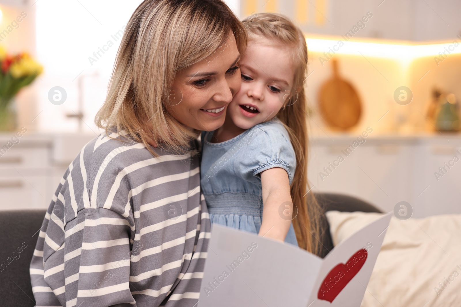 Photo of Little daughter congratulating her mom with greeting card at home. Happy Mother's Day