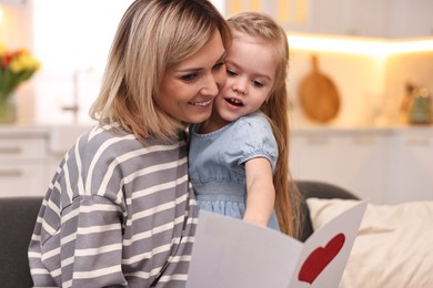 Photo of Little daughter congratulating her mom with greeting card at home. Happy Mother's Day