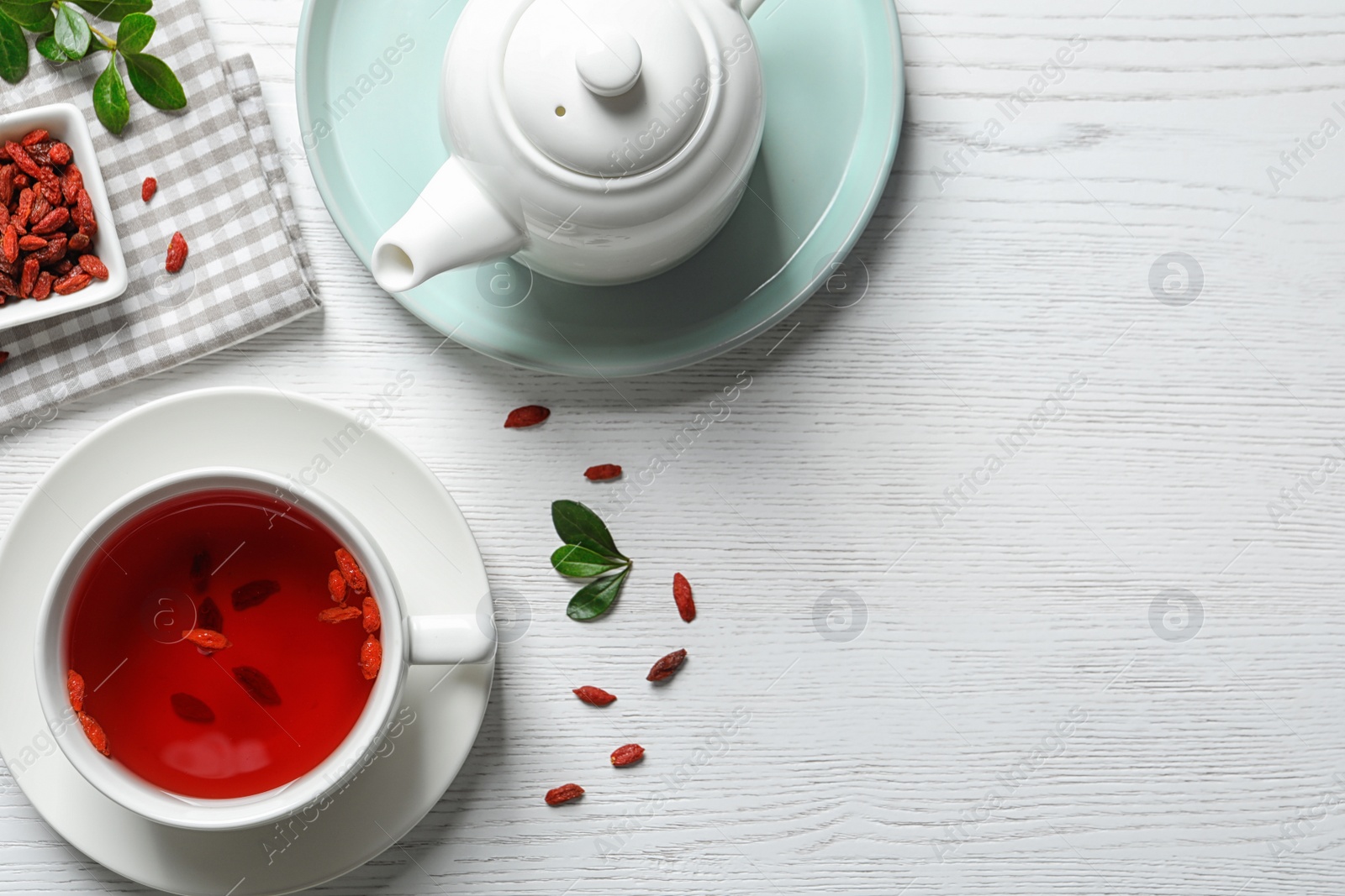 Photo of Healthy goji tea in cup served on white wooden table, flat lay. Space for text