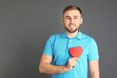 Young man with paper heart on grey background. Space for text