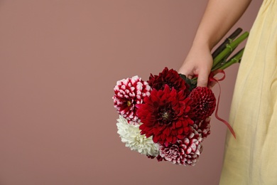 Photo of Woman with bouquet of beautiful dahlia flowers on brown background, closeup. Space for text