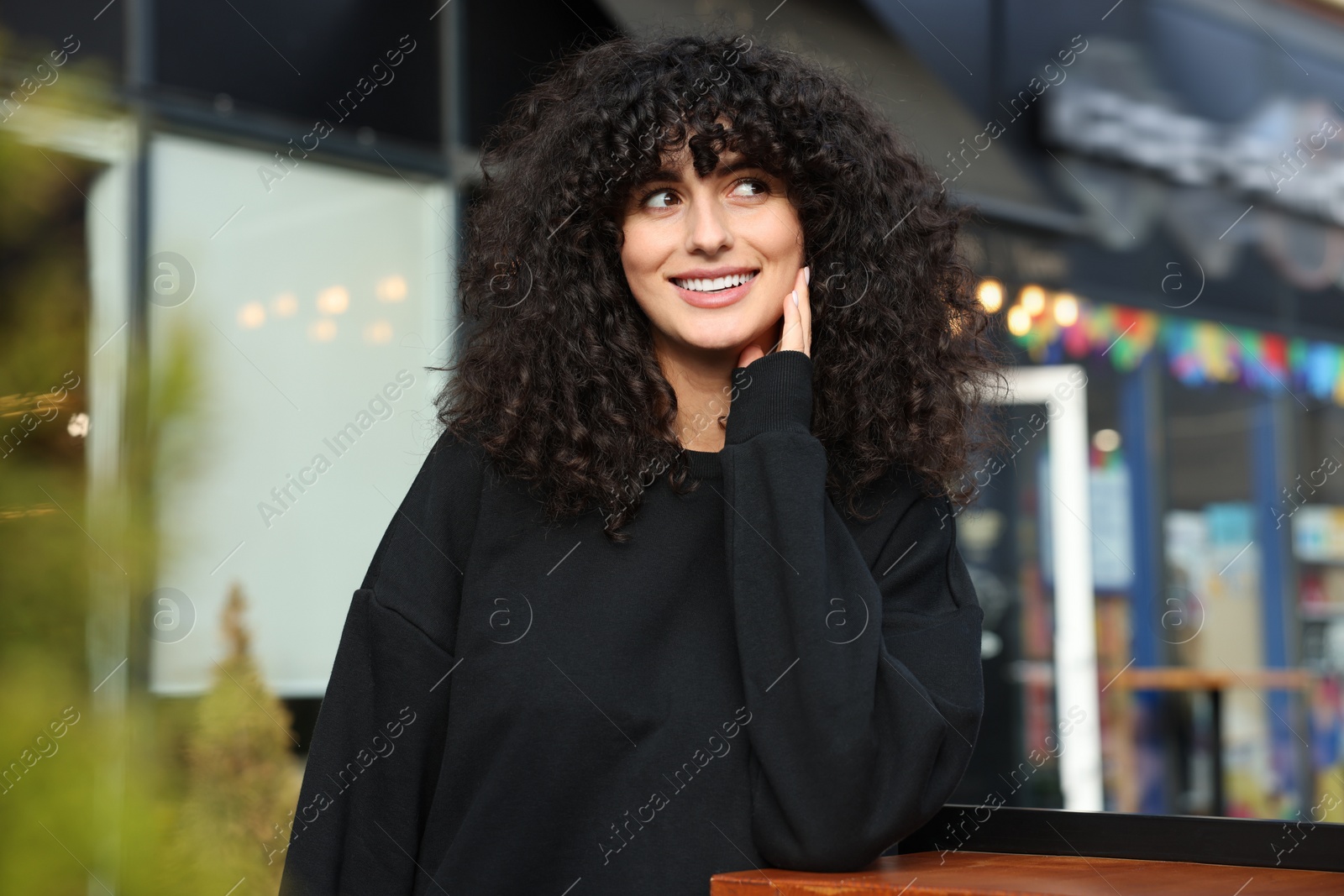 Photo of Happy young woman in stylish black sweater at wooden table outdoors