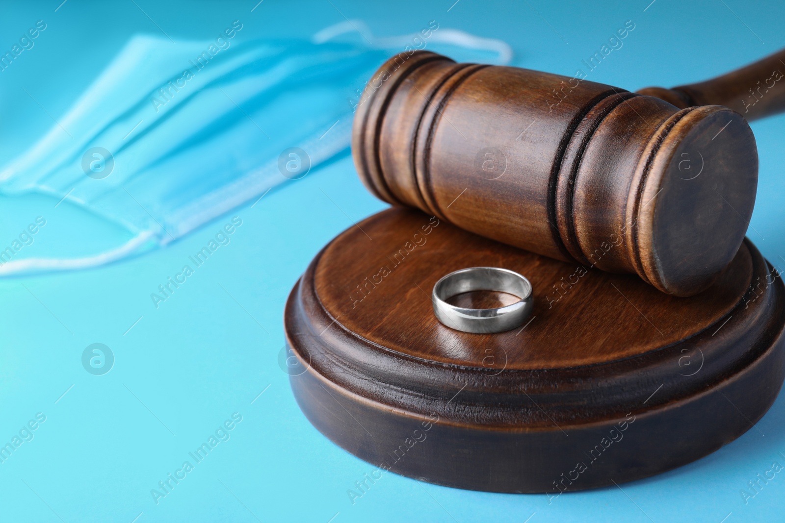 Photo of Wedding ring and judge hammer on light blue background, closeup. Divorce during coronavirus outbreak
