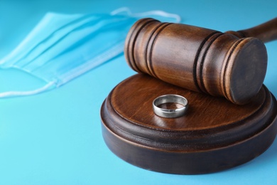 Photo of Wedding ring and judge hammer on light blue background, closeup. Divorce during coronavirus outbreak