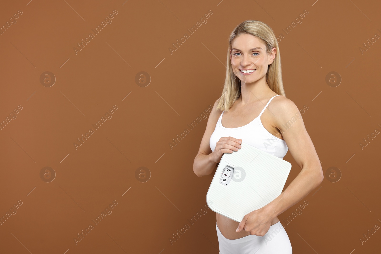 Photo of Slim woman holding scales on brown background, space for text. Weight loss