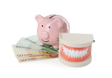 Photo of Educational dental typodont model, piggy bank and euro banknotes on white background. Expensive treatment
