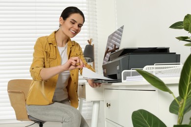 Woman using modern printer at workplace indoors