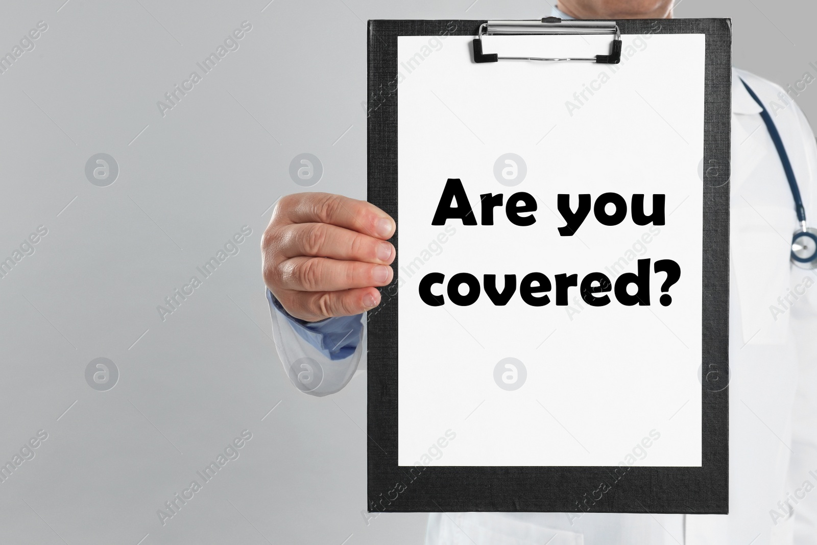 Image of Doctor holding clipboard with text ARE YOU COVERED? on light background, closeup. Insurance concept