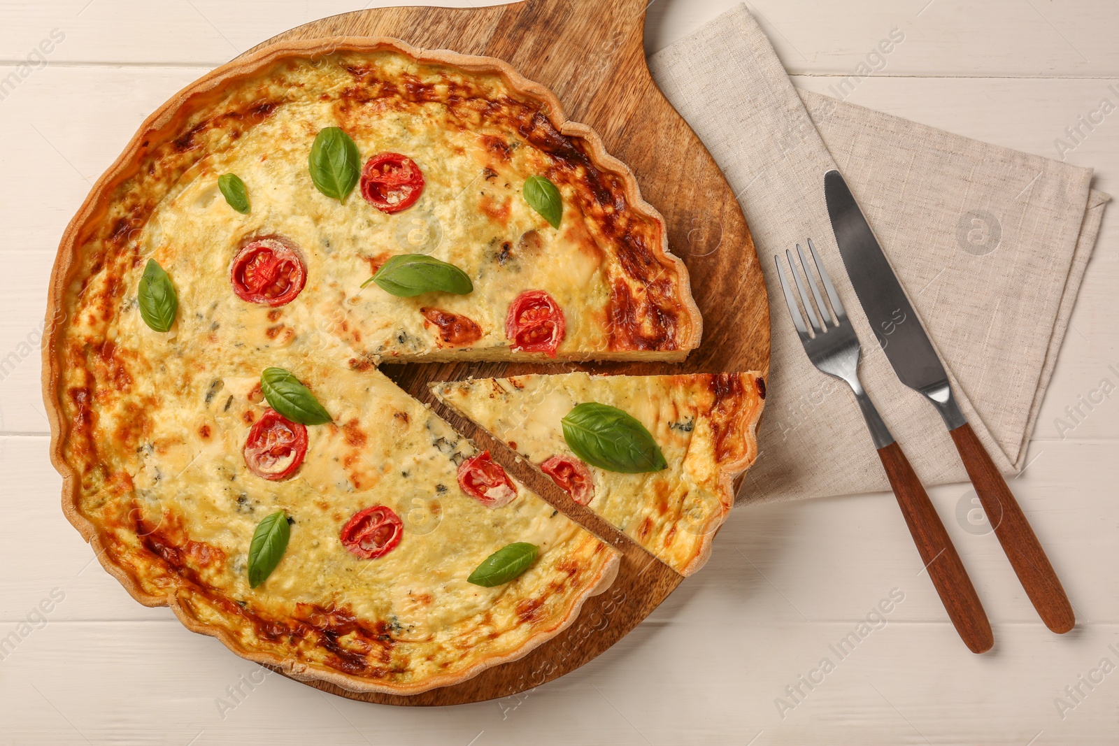 Photo of Delicious homemade cheese quiche and cutlery on white wooden table, flat lay