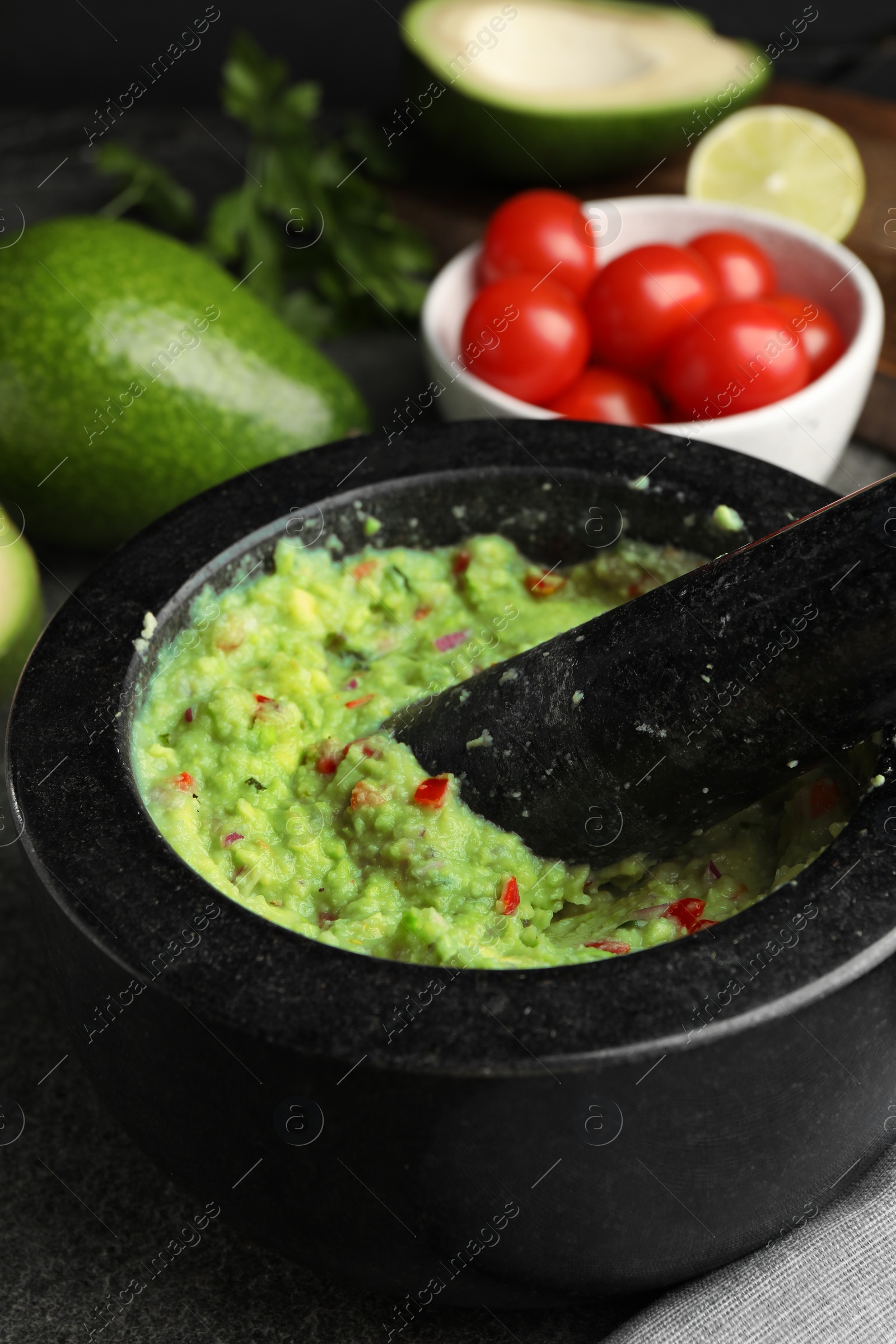 Photo of Mortar with delicious guacamole and ingredients on table