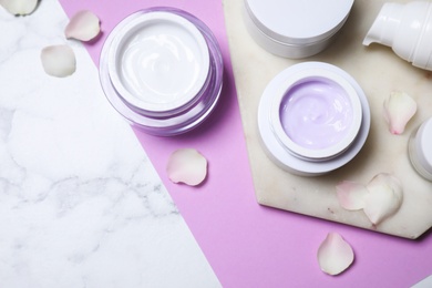 Flat lay composition with different skin care products and petals on white marble background, space for text