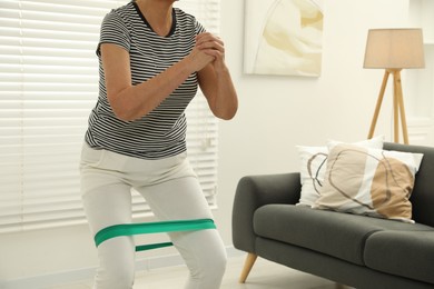 Photo of Senior woman doing squats with fitness elastic band at home, closeup. Space for text