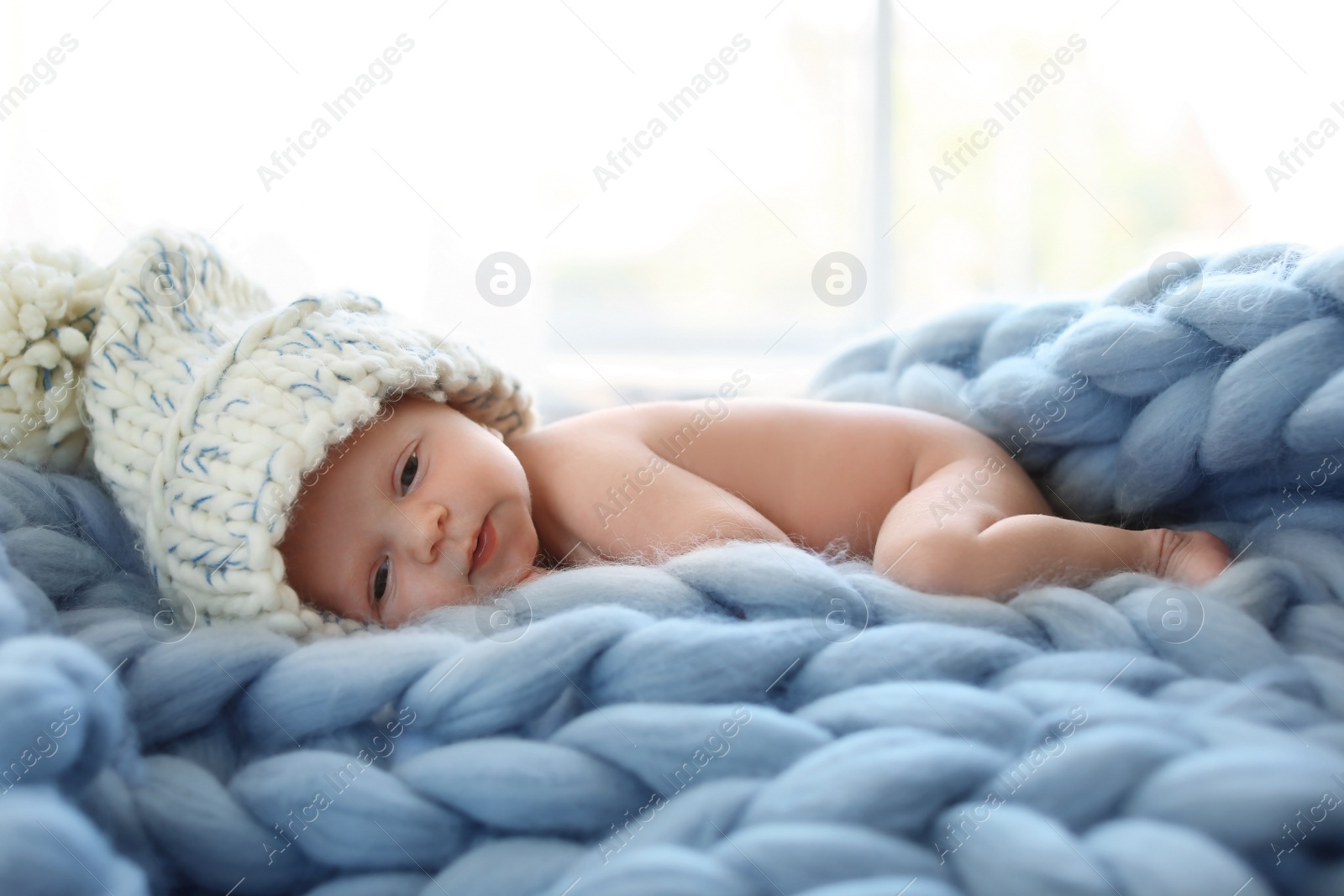 Photo of Adorable newborn baby in big hat lying on knitted blanket indoors