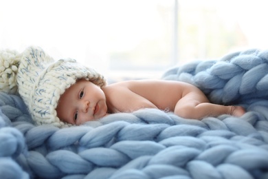 Adorable newborn baby in big hat lying on knitted blanket indoors