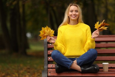 Photo of Happy woman with autumn leaves on bench in park. Space for text