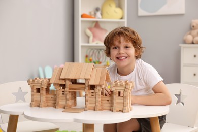 Photo of Little boy playing with wooden entry gate at white table in room. Child's toy