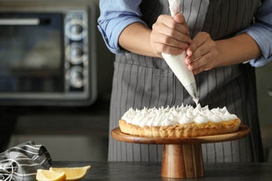 Woman preparing lemon meringue pie at table in kitchen, closeup