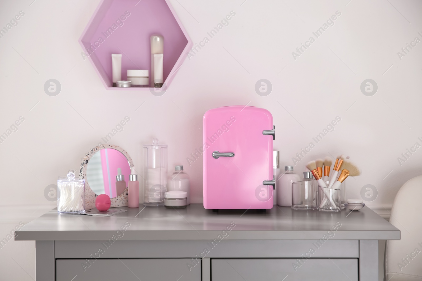 Photo of Cosmetics refrigerator and skin care products on grey chest of drawers indoors