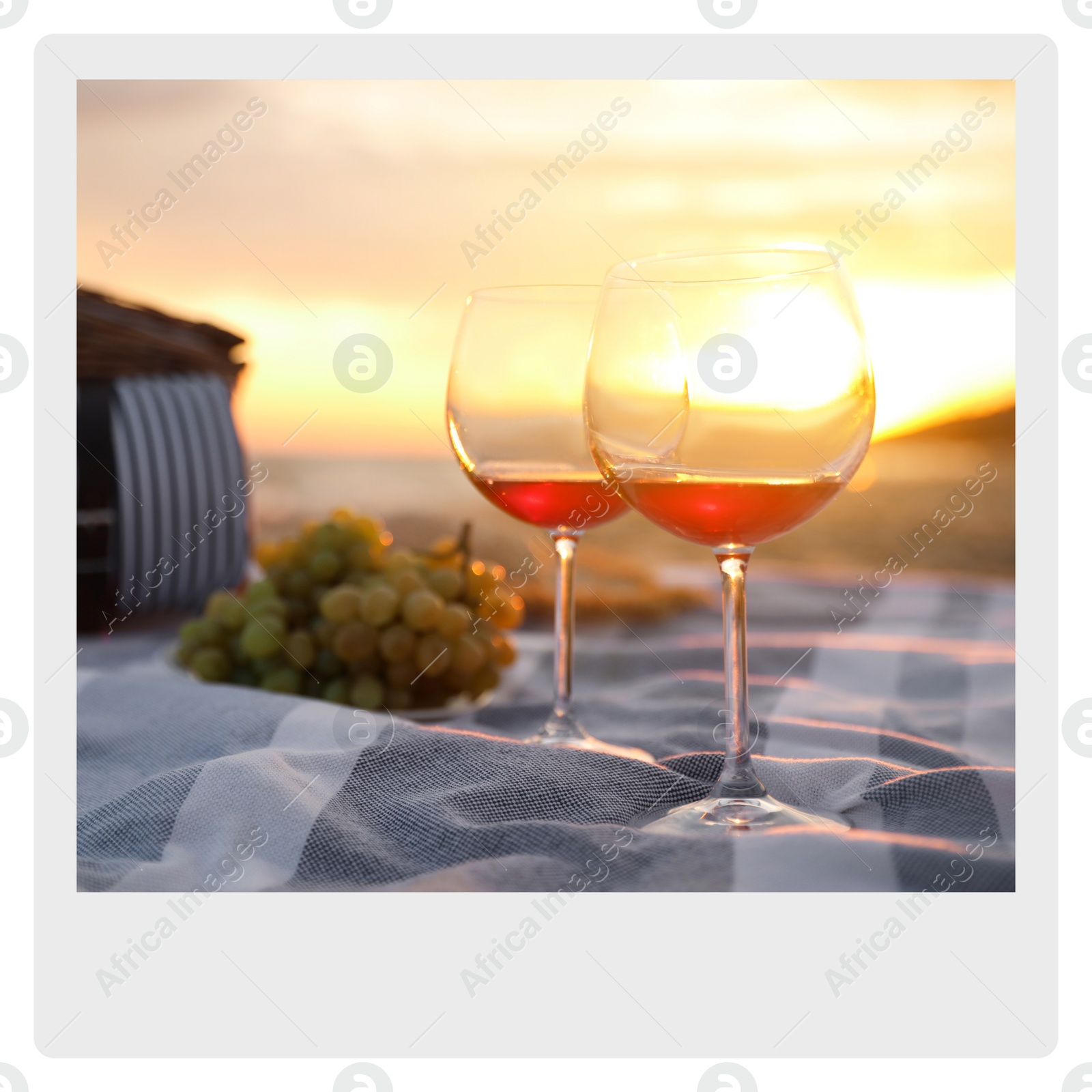 Image of Paper photo. Blanket with glasses of wine and food on beach at sunset 