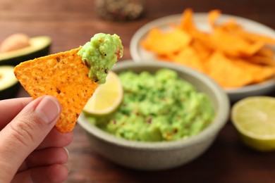 Woman holding delicious nachos chip with guacamole at wooden table, closeup. Space for text