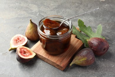 Jar of tasty sweet jam, fresh figs and green leaf on grey table, flat lay