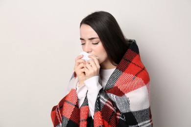 Photo of Young woman with blanket suffering from runny nose on beige background