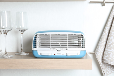 Photo of Modern air purifier and glasses on wooden shelf in kitchen