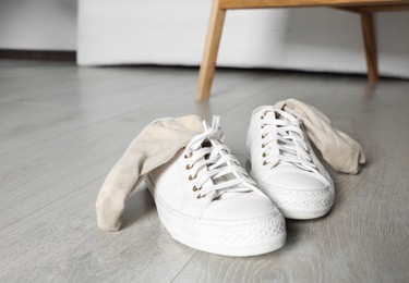 Photo of Sneakers with dirty socks on white wooden floor indoors