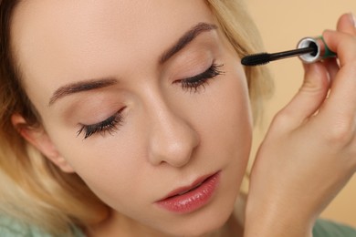 Beautiful woman applying mascara on beige background, closeup