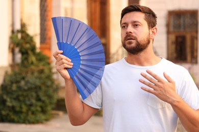 Photo of Man with hand fan suffering from heat outdoors