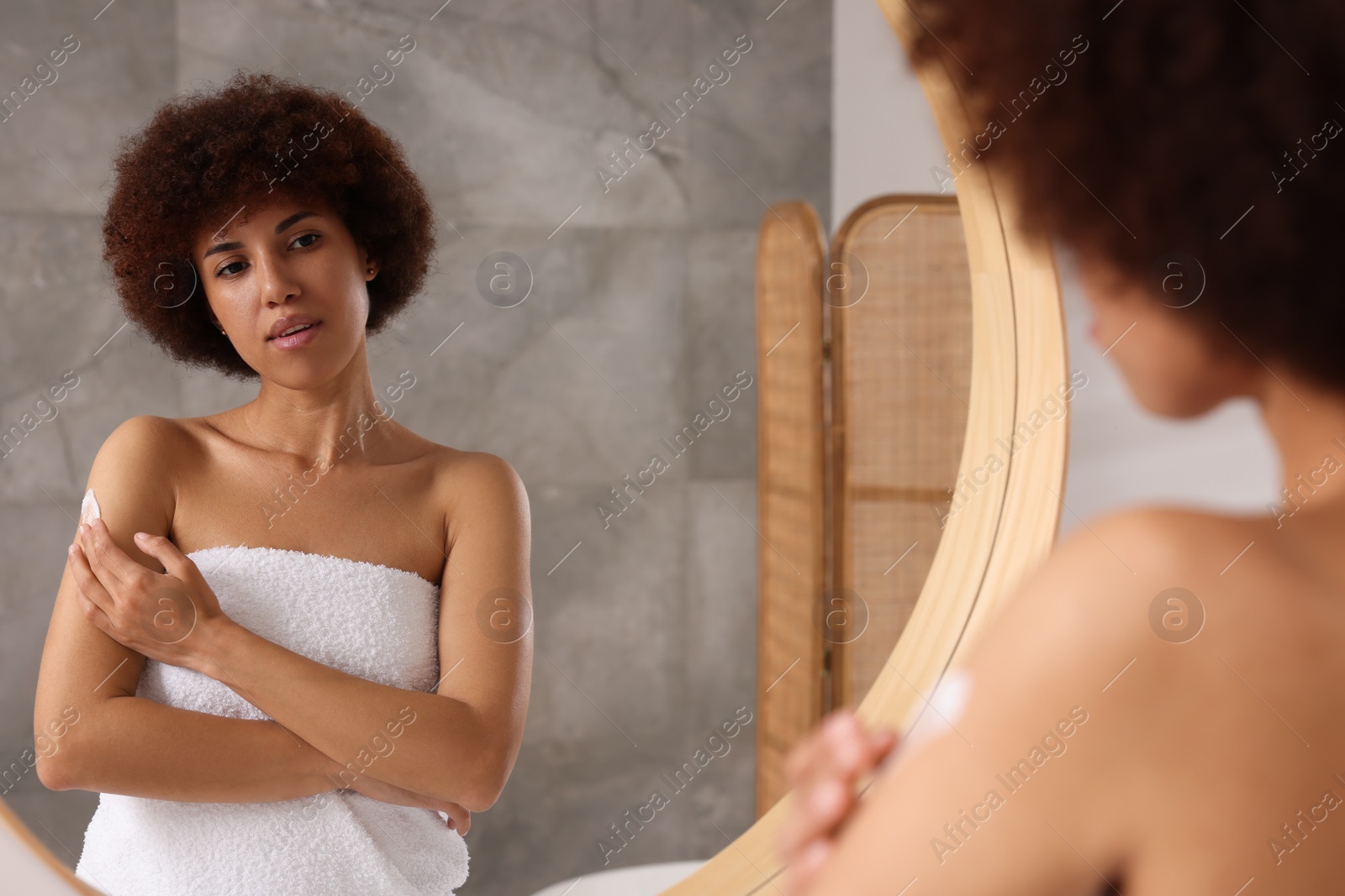 Photo of Beautiful young woman applying body cream onto arm indoors