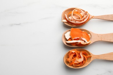 Spoons with dry orange peels on white marble table, flat lay. Space for text