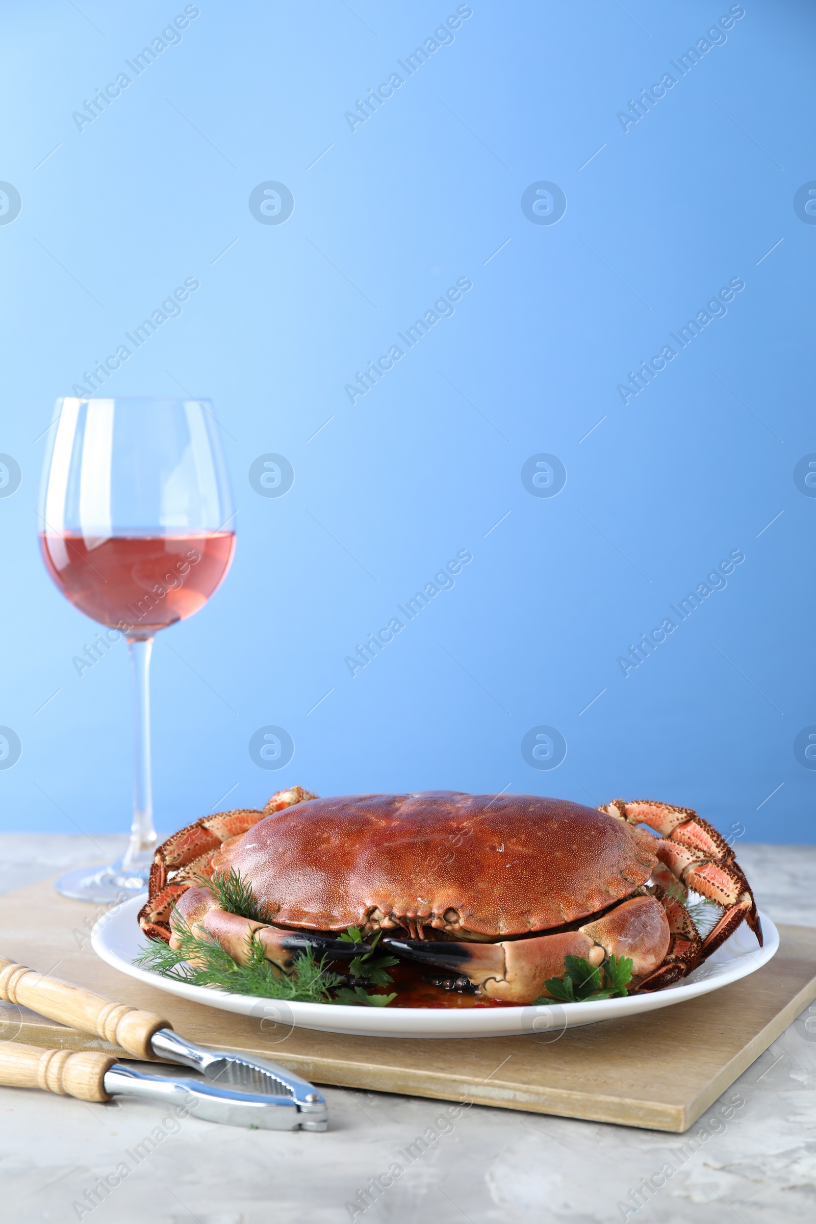 Photo of Delicious crab served with greens and wine on table against light blue background. Space for text